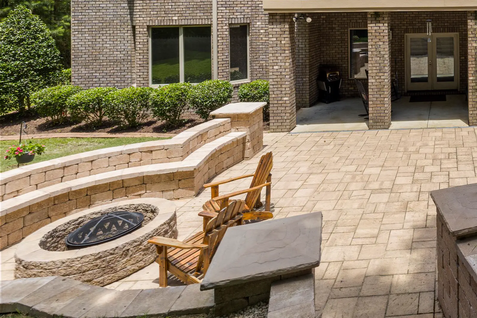 A round stone fire pit set into a curved seat wall on a stone patio, with two Adirondack chairs