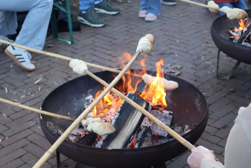 Marshmallows on sticks toasting over a steel fire bowl on brick pavers